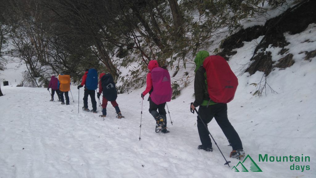 寒い中レインウェアやハードシェルを着て歩く登山者たちの写真